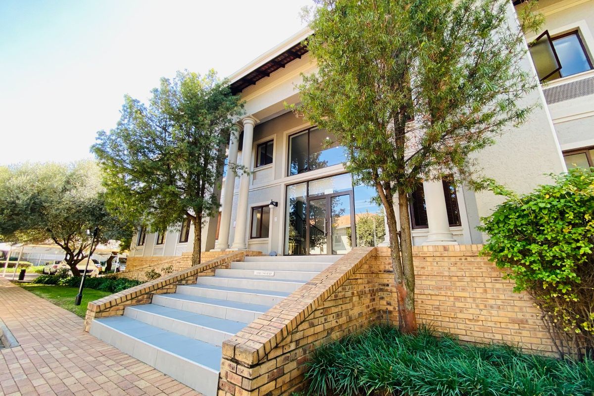 Front exterior view of a commercial building featuring a grand entrance with classical columns, a tiled staircase, and brick architectural detailing.