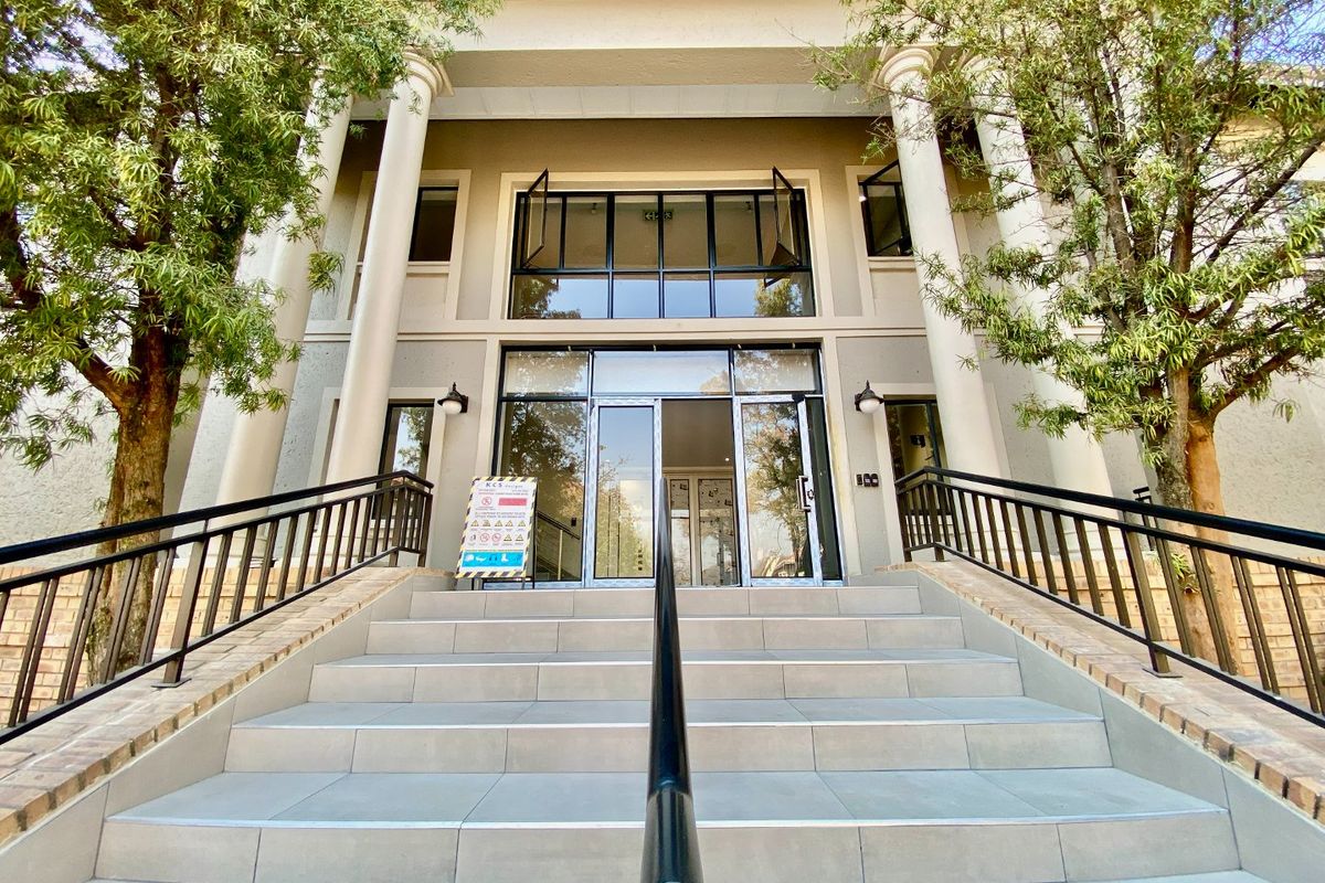 A professional commercial building entrance featuring a wide tiled staircase, classical columns, and modern glass double doors with metal handrails.