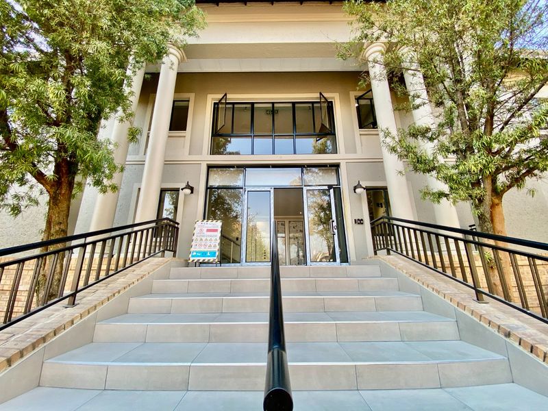 A professional commercial building entrance featuring a wide tiled staircase, classical columns, and modern glass double doors with metal handrails.