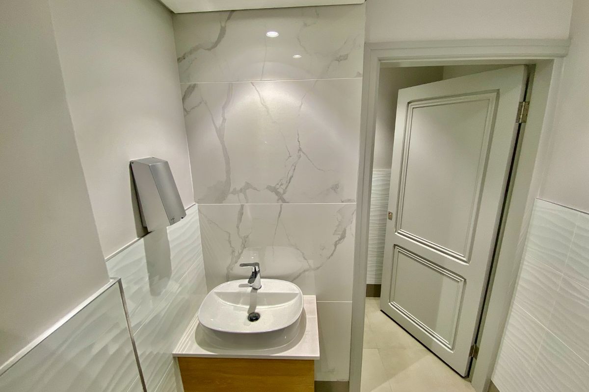 A modern, well-maintained bathroom featuring a vessel sink on a wooden vanity, complemented by elegant marble-look and textured wall tiling.