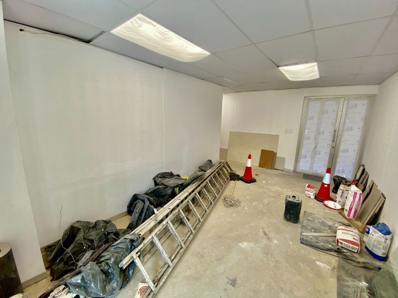 An empty commercial office space currently undergoing renovation, featuring a suspended ceiling, recessed lighting, and a glass entrance door.