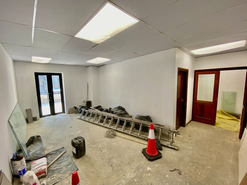 An empty commercial office space featuring a suspended ceiling with recessed lighting, concrete flooring, and access via a double glass door.