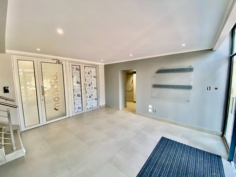 A clean and modern commercial building entrance lobby featuring tiled floors, recessed lighting, and glass entry doors with clear directional signage.