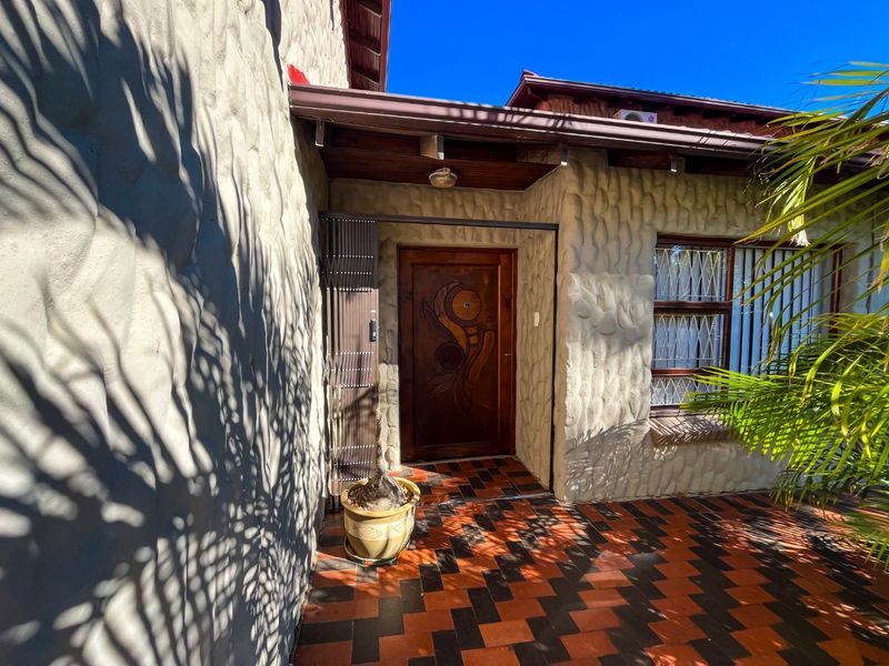 Front entrance area featuring textured wall cladding, a decorative timber door, security gate, and patterned tiled flooring under a covered patio.