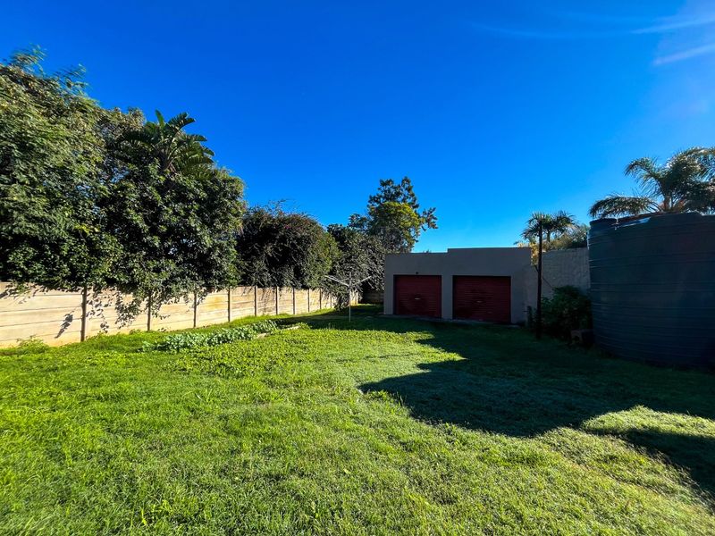 A spacious rear garden featuring a lawn, precast concrete boundary walls, a double garage, and a large water storage tank.
