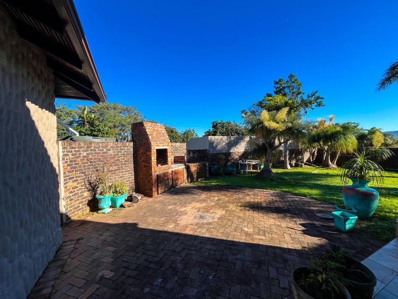 Outdoor patio area featuring a built-in brick braai, paved flooring, and a surrounding brick boundary wall, set within a garden space.