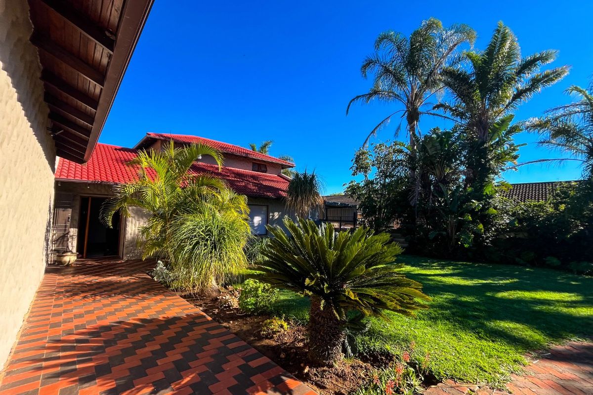 A view of the rear exterior featuring a covered tiled patio, red roof tiles, and a well-maintained garden with established landscaping.