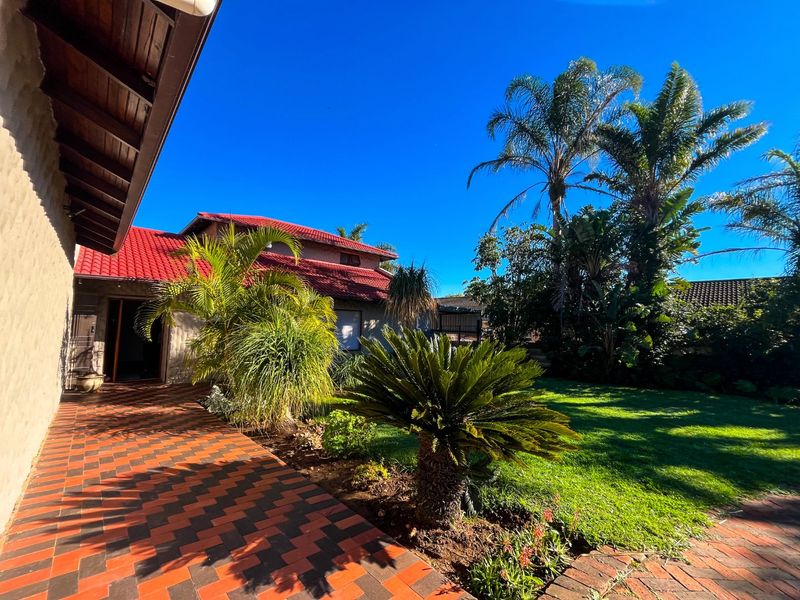 A view of the rear exterior featuring a covered tiled patio, red roof tiles, and a well-maintained garden with established landscaping.