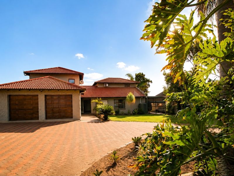 Front view of a well-maintained house featuring a paved driveway, double garage, and terracotta tiled roof set within a landscaped garden.