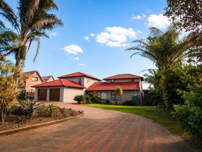 A well-maintained residential property featuring a paved driveway, double garage, and a landscaped garden with mature palm trees.