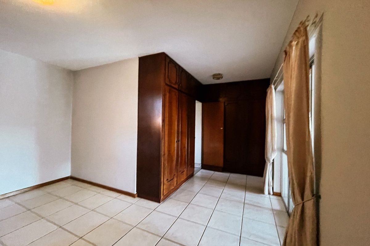 A spacious bedroom featuring built-in wooden cupboards, tiled flooring, and a sliding glass door providing natural light.