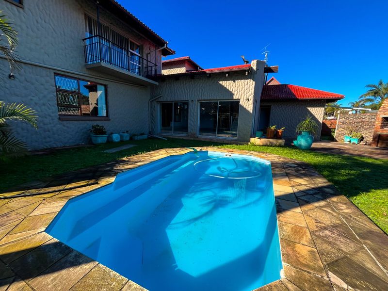 Rear exterior view featuring a swimming pool with stone coping, a balcony, and sliding glass doors leading into the home.
