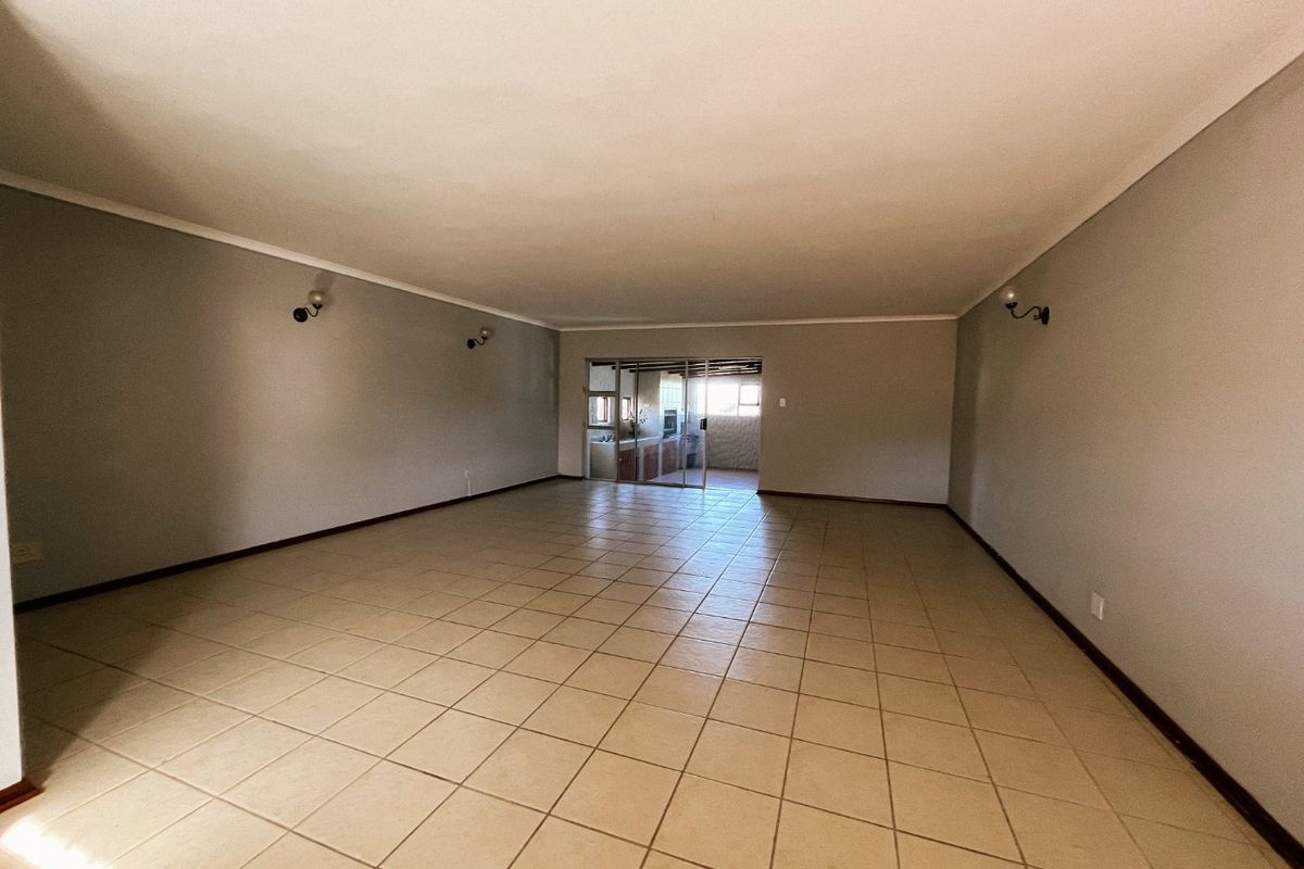 A spacious, empty living area featuring neutral ceramic floor tiles, wall-mounted lighting, and a sliding glass door leading to an adjacent room.