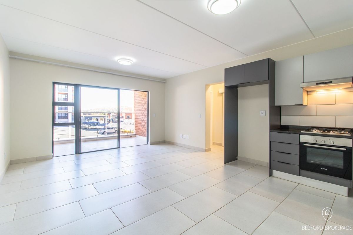 Modern open-plan living area featuring tiled floors, a sleek kitchen with built-in appliances, and a sliding door leading to a balcony.