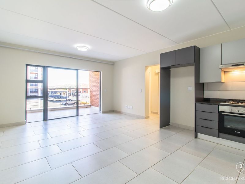 Modern open-plan living area featuring tiled floors, a sleek kitchen with built-in appliances, and a sliding door leading to a balcony.