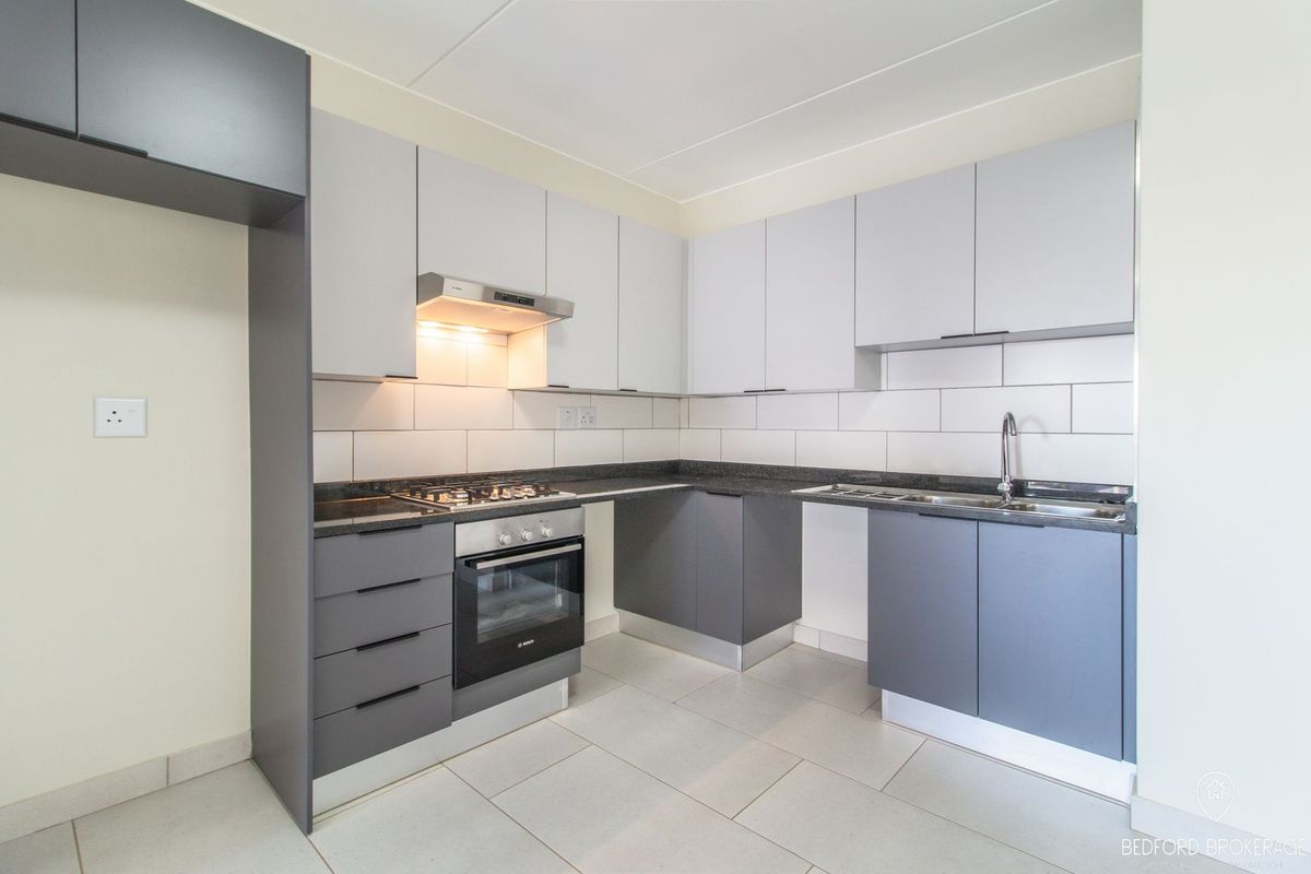Modern kitchen featuring grey and white cabinetry, stone countertops, built-in oven, gas hob, and tiled backsplash in a clean, contemporary layout.