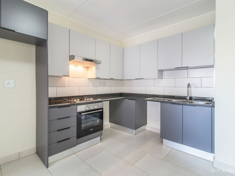 Modern kitchen featuring grey and white cabinetry, stone countertops, built-in oven, gas hob, and tiled backsplash in a clean, contemporary layout.