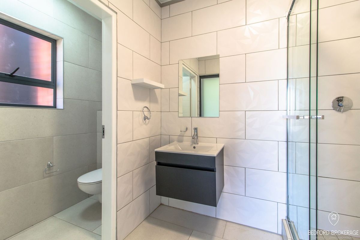 Modern bathroom featuring a wall-mounted vanity, glass shower enclosure, and a separate toilet area with contemporary tiled finishes.