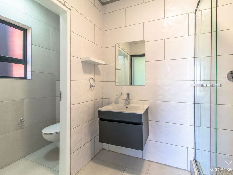 Modern bathroom featuring a wall-mounted vanity, glass shower enclosure, and a separate toilet area with contemporary tiled finishes.