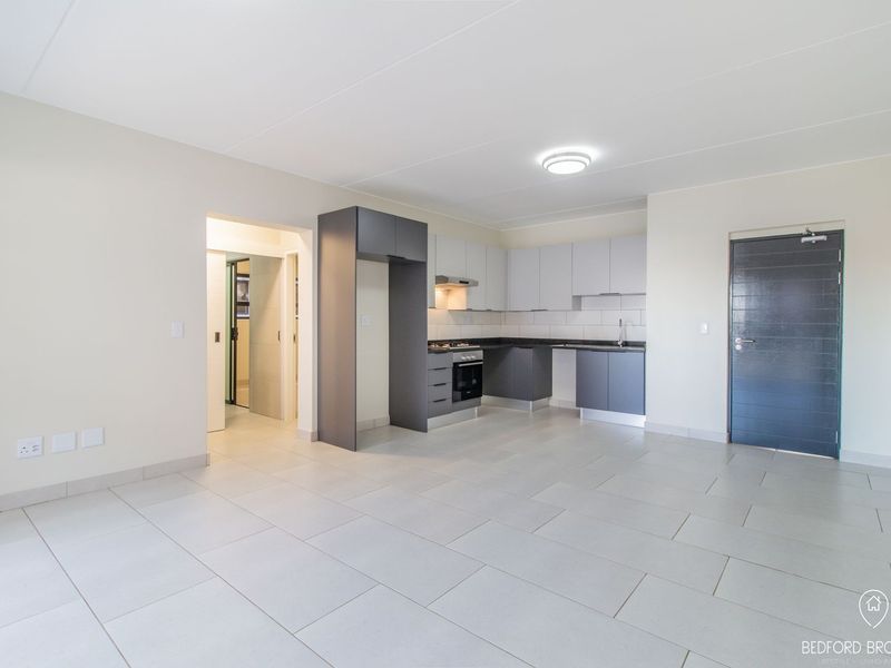 Modern open-plan kitchen and living area featuring sleek cabinetry, built-in appliances, and neutral tiled flooring in a clean, vacant space.