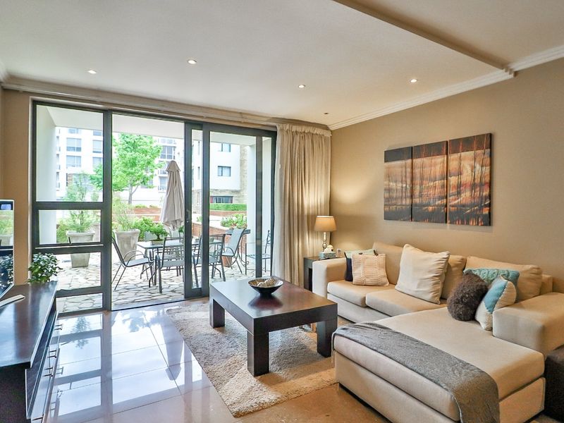 A well-maintained living room featuring tiled flooring, recessed ceiling lights, and large sliding glass doors that provide direct access to an outdoor patio area.