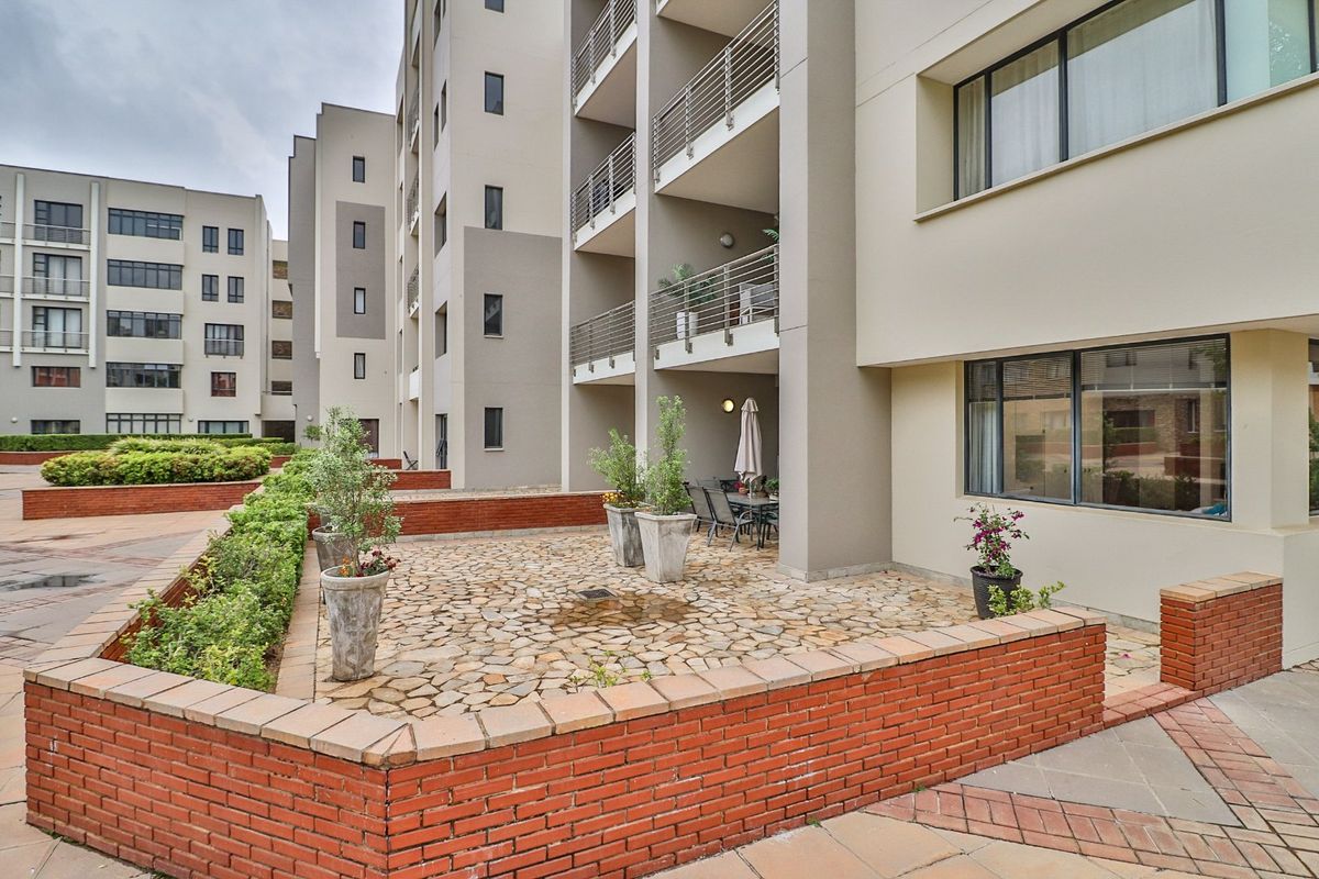 Ground floor patio area with stone paving and brick retaining walls, featuring access to the apartment building with balconies above.