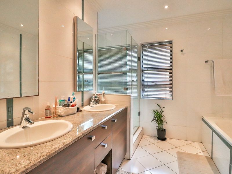 Modern bathroom featuring a double vanity with granite countertops, built-in cabinetry, a glass-enclosed shower, and a separate bathtub with tiled finishes.