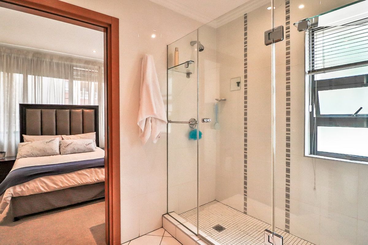 A modern bathroom featuring a glass-enclosed shower with tiled finishes, adjacent to a bedroom entrance.