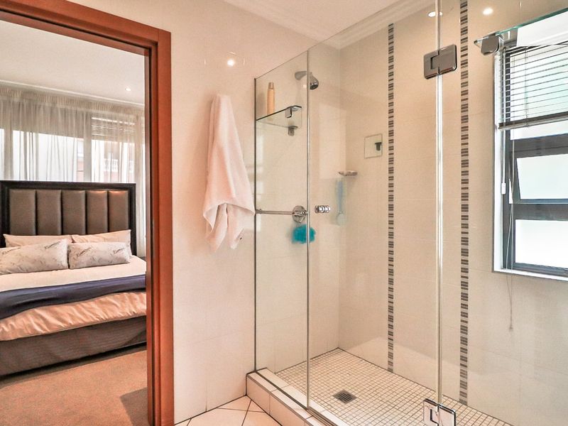 A modern bathroom featuring a glass-enclosed shower with tiled finishes, adjacent to a bedroom entrance.