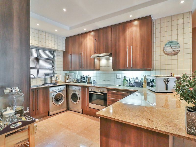 A well-appointed kitchen featuring dark wood cabinetry, granite countertops, integrated appliances, and a tiled backsplash with recessed lighting.