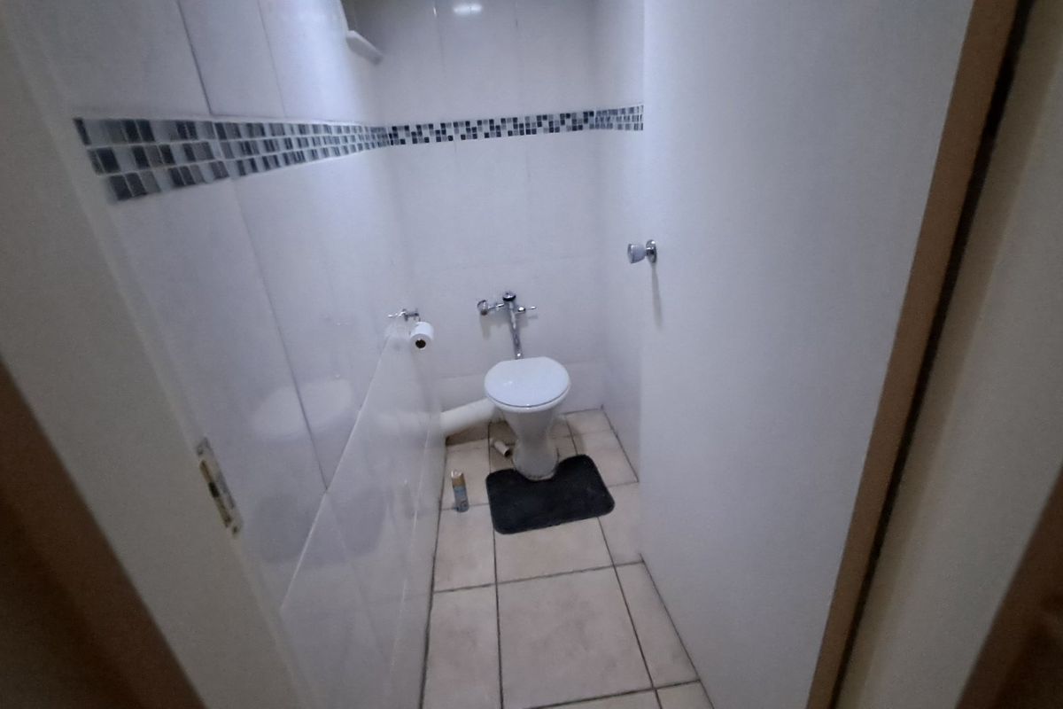 A compact bathroom featuring tiled walls with a mosaic border and a standard toilet, currently in need of minor cosmetic updates.