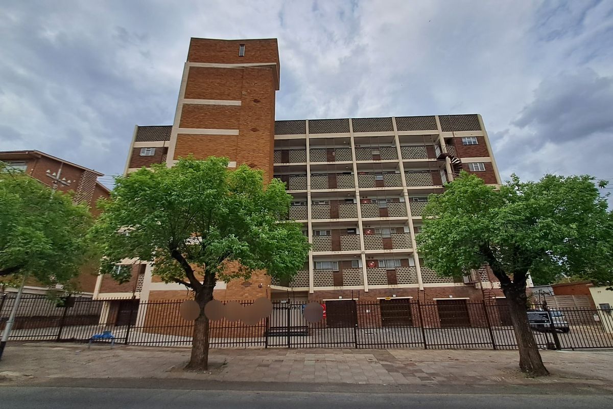 Front elevation of a multi-story apartment building featuring brick construction, security fencing, and external balcony access.