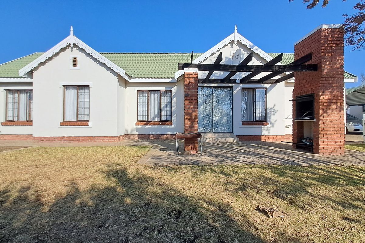 Rear view of the townhouse featuring a paved patio area with a built-in brick braai, timber pergola, and access to the garden.
