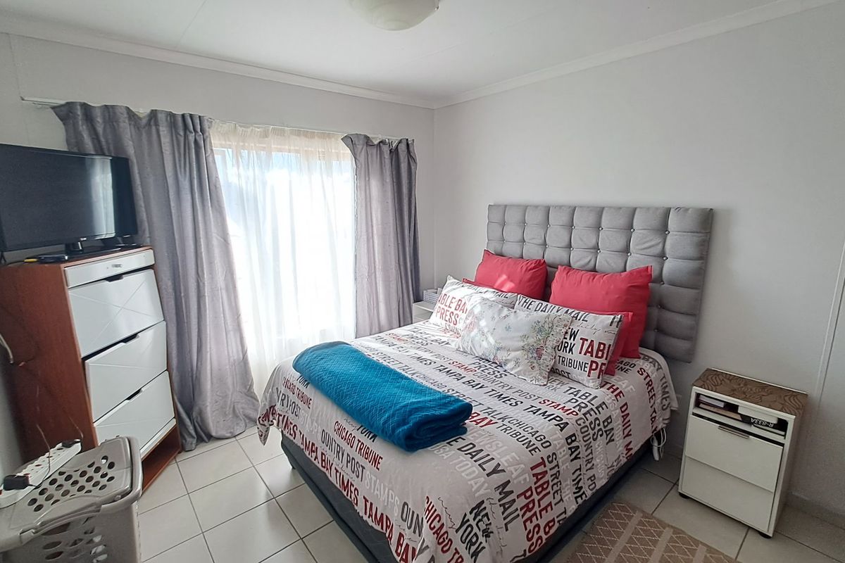 A functional bedroom featuring tiled flooring and large windows with curtain rails, providing a bright and comfortable living space.