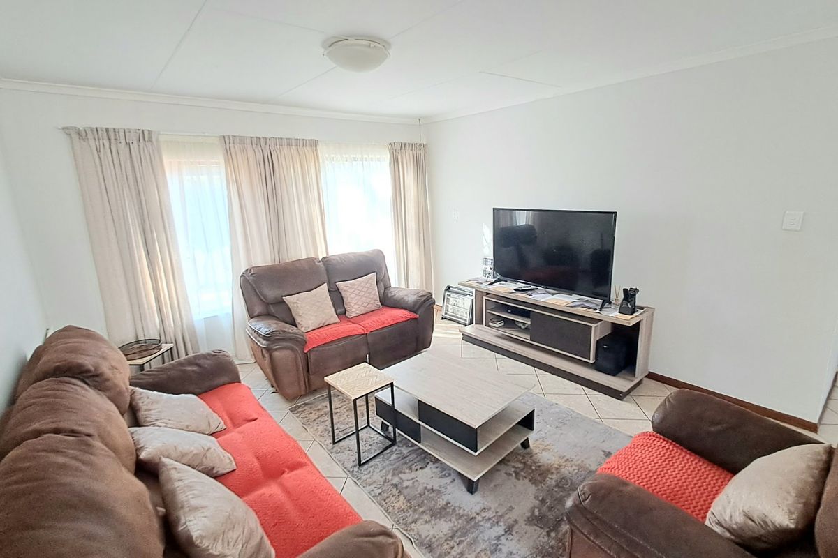 A spacious living room featuring neutral tiled flooring and large windows with curtains, providing a bright and comfortable area for relaxation.