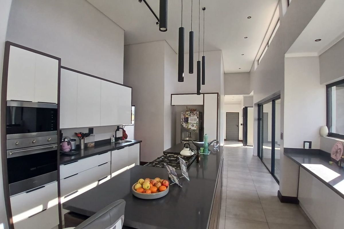 Modern kitchen featuring sleek white cabinetry, dark stone countertops, a central island with gas hob, and high ceilings with contemporary pendant lighting.