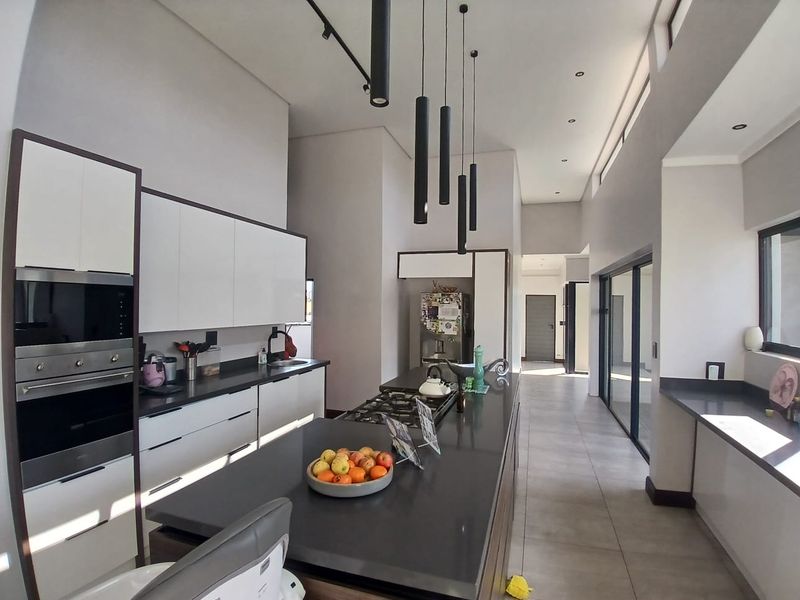 Modern kitchen featuring sleek white cabinetry, dark stone countertops, a central island with gas hob, and high ceilings with contemporary pendant lighting.
