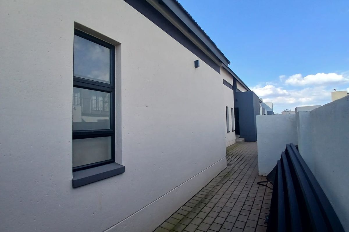 A clean side passage featuring paved flooring, modern white exterior walls with dark trim, and aluminium window frames.