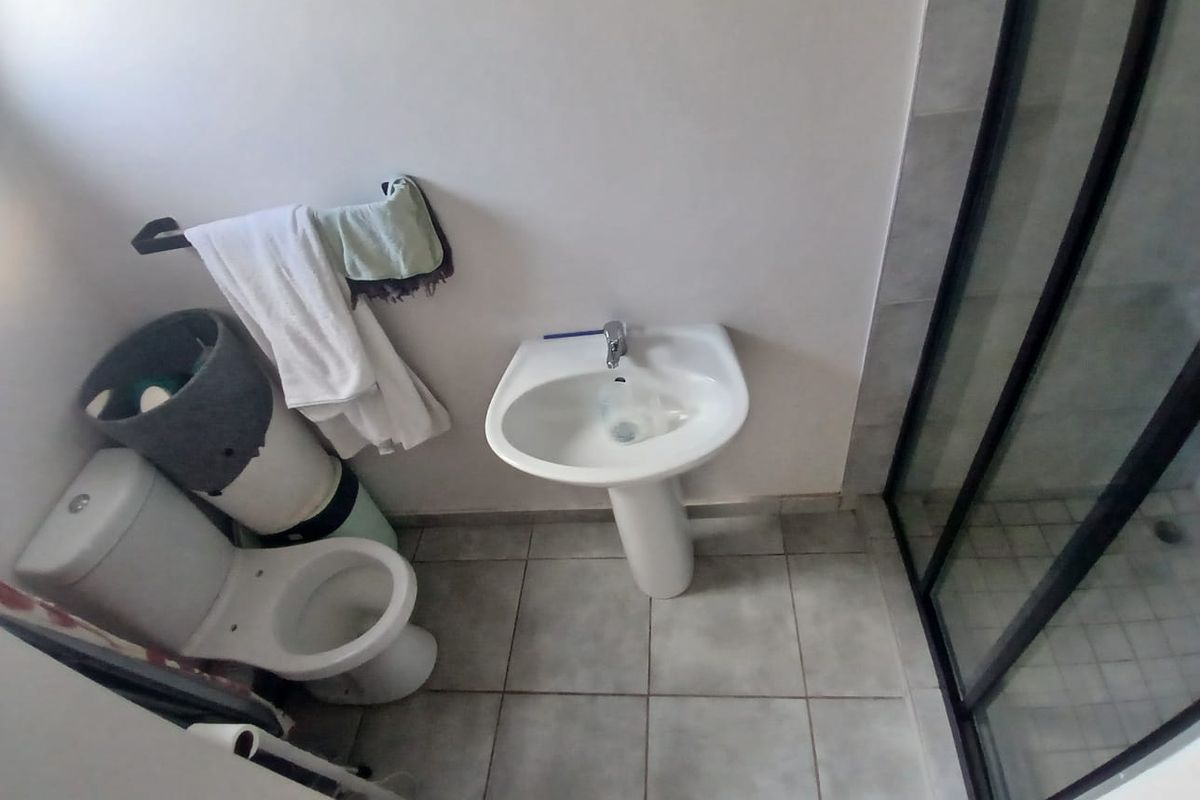 A functional bathroom featuring a pedestal washbasin, toilet, and a shower enclosure with tiled flooring.