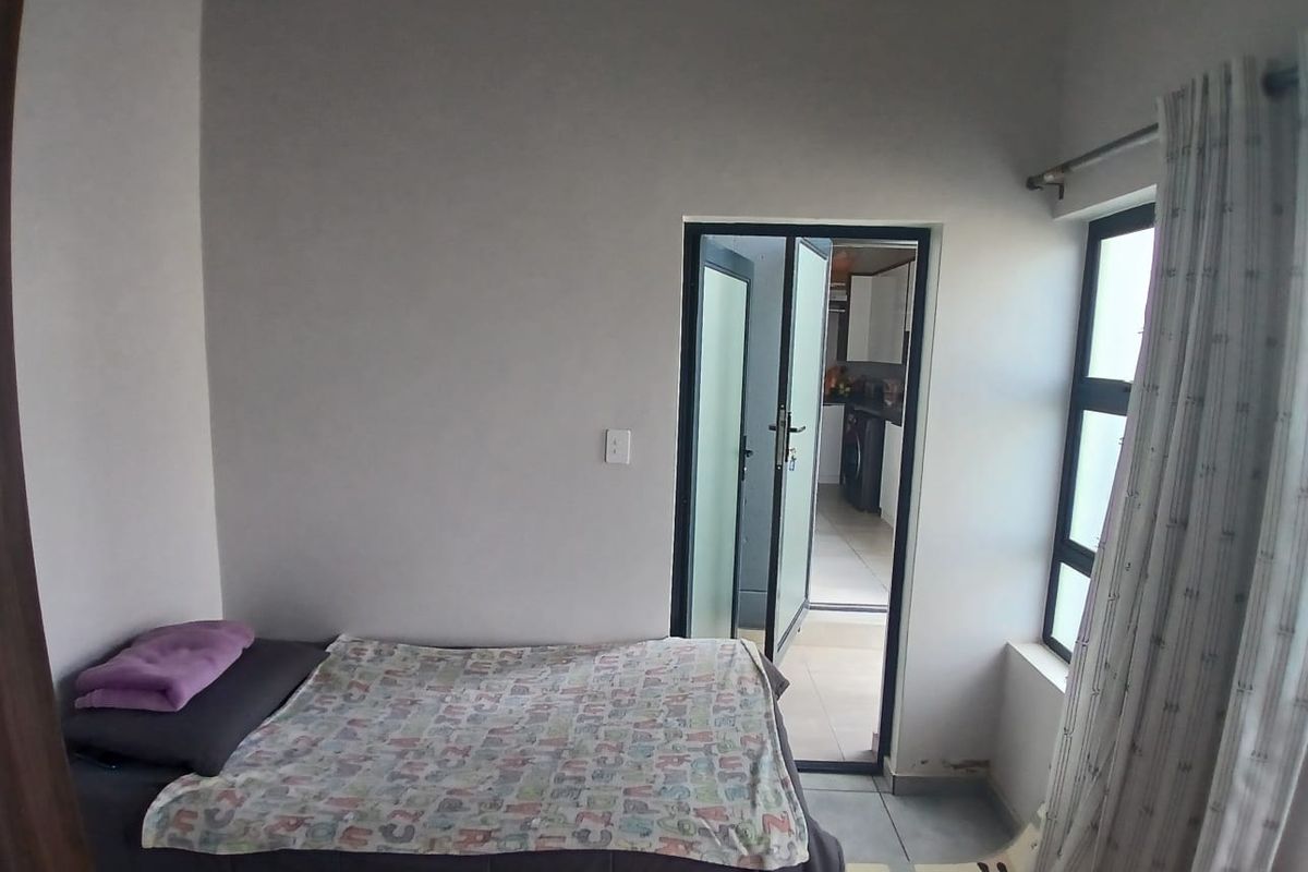 A compact bedroom featuring tiled flooring and an aluminium door leading to an adjacent space, showing signs of wear on the lower wall sections.