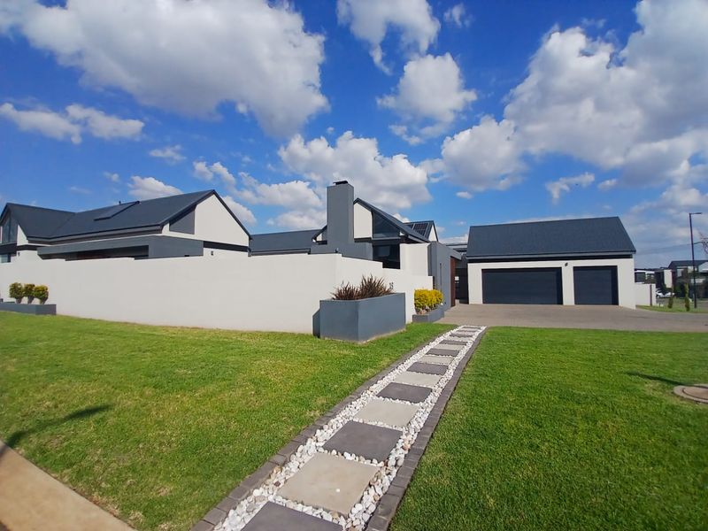 Modern contemporary house exterior featuring a double garage, paved driveway, landscaped lawn, and a stone pathway leading to the entrance.