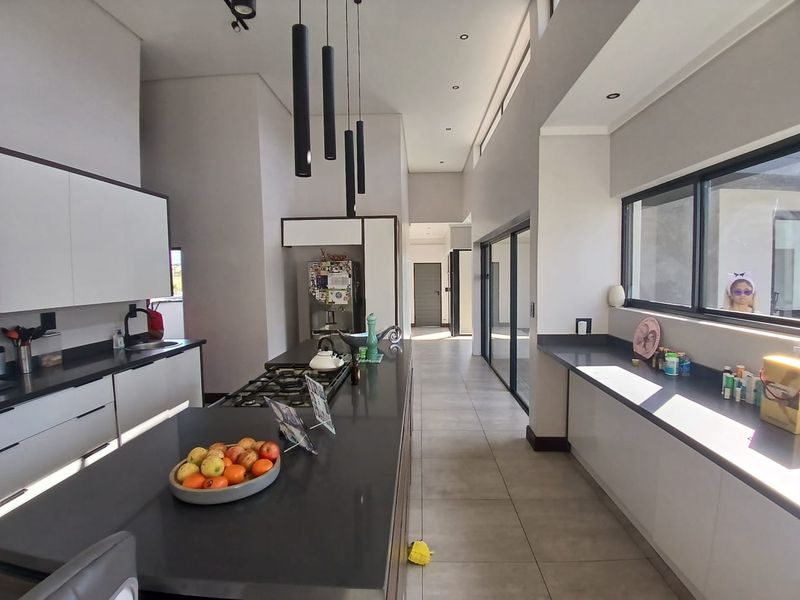 Modern kitchen featuring a large central island with gas cooktop, sleek cabinetry, stone countertops, and expansive sliding doors leading to the outdoor area.