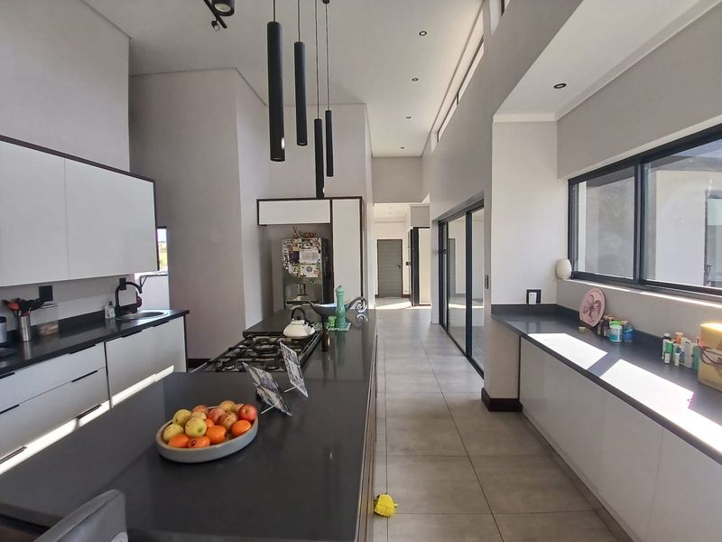 Modern kitchen featuring a large central island with gas hob, sleek cabinetry, stone countertops, and expansive sliding doors leading to the exterior.