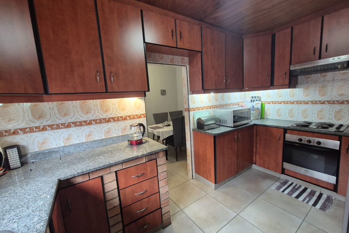 A functional kitchen featuring wood-finish cabinetry, granite countertops, built-in oven with hob, and tiled backsplash, offering a classic layout with ample storage space.