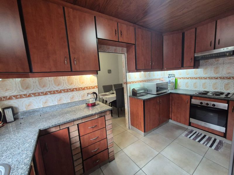A functional kitchen featuring wood-finish cabinetry, granite countertops, built-in oven with hob, and tiled backsplash, offering a classic layout with ample storage space.