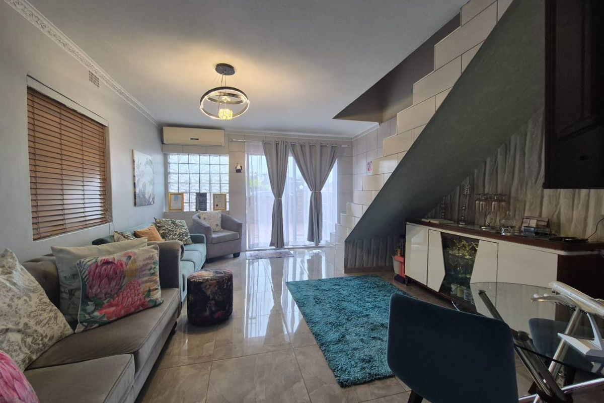 A well-maintained living room featuring polished tile flooring, crown molding, a staircase, and a split-system air conditioner with access to an outdoor area.