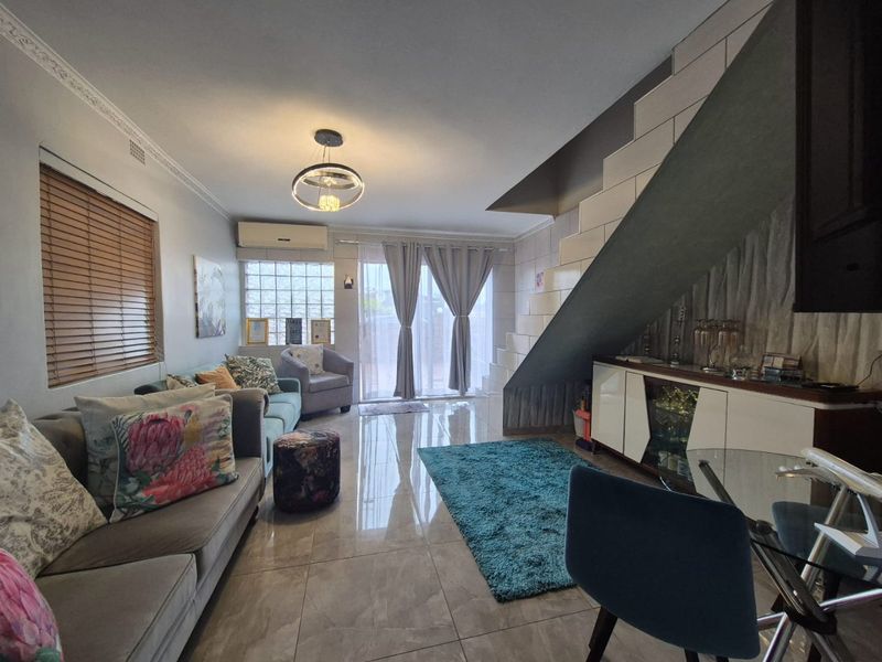 A well-maintained living room featuring polished tile flooring, crown molding, a staircase, and a split-system air conditioner with access to an outdoor area.