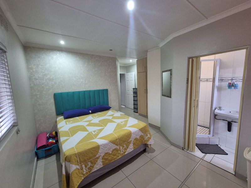 A well-maintained bedroom featuring tiled flooring, recessed lighting, built-in cupboards, and an attached en-suite bathroom with a folding door.