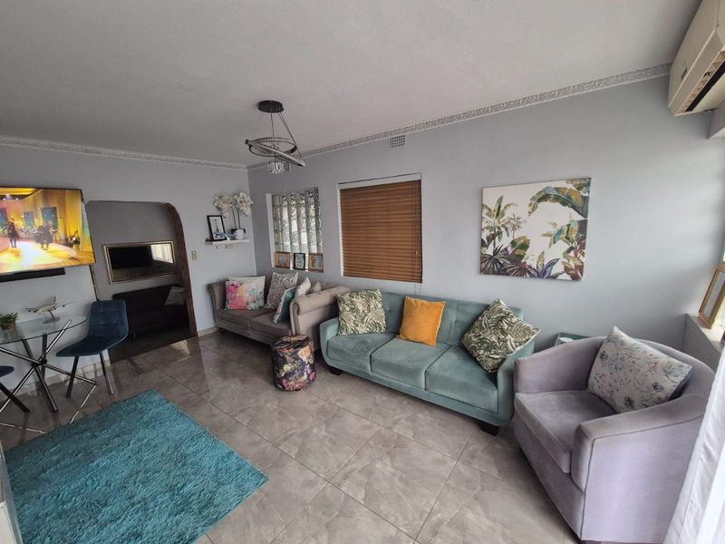 A well-maintained living room featuring tiled flooring, decorative crown molding, and a glass block feature window, providing a bright and comfortable living space.