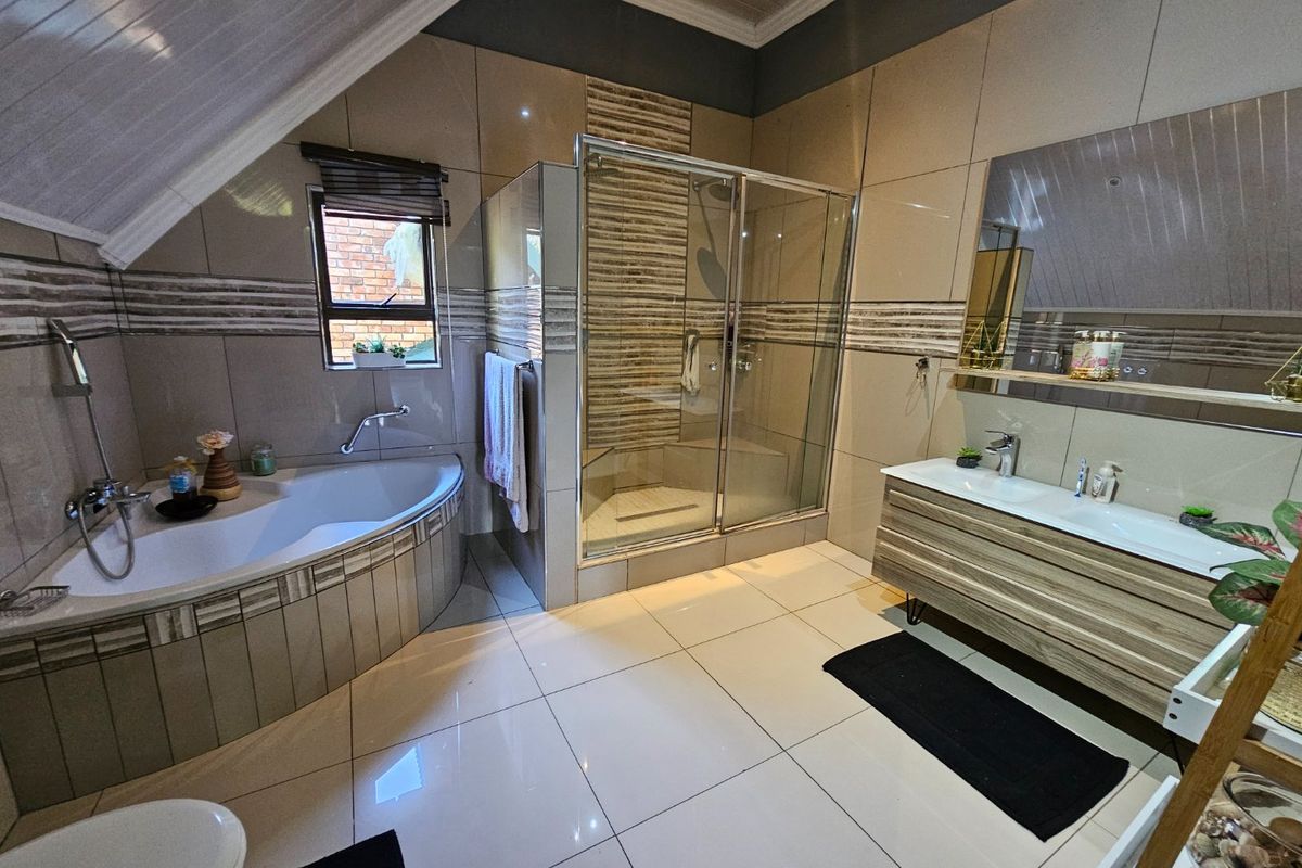 Modern bathroom featuring a corner bathtub, glass-enclosed shower, and a contemporary vanity unit with integrated basin, finished with neutral wall and floor tiling.